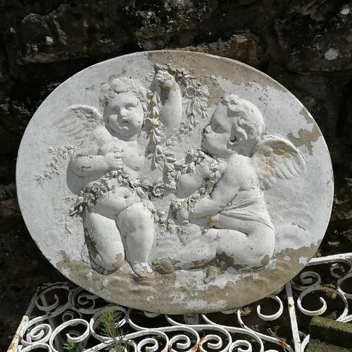 10 - Oval wall plaque depicting cherubs with a garland 66cm x 56cm - some losses to the paint finish