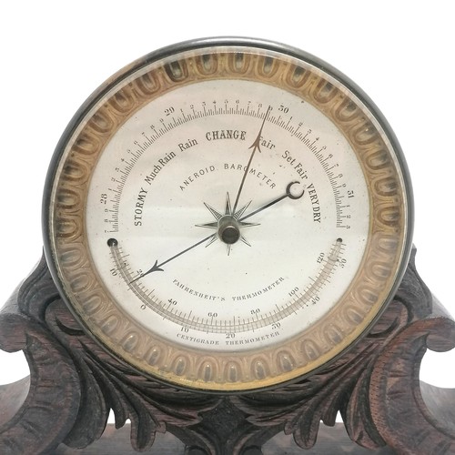 208 - Antique aneroid barometer with curved thermometer on hand carved oak stand - 21cm high x 32cm wide x... 