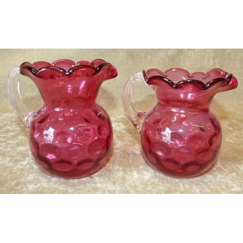 94 - 2 Cranberry Bulbous Shape Jugs having scalloped rims with clear reeded handles, 13cm high  