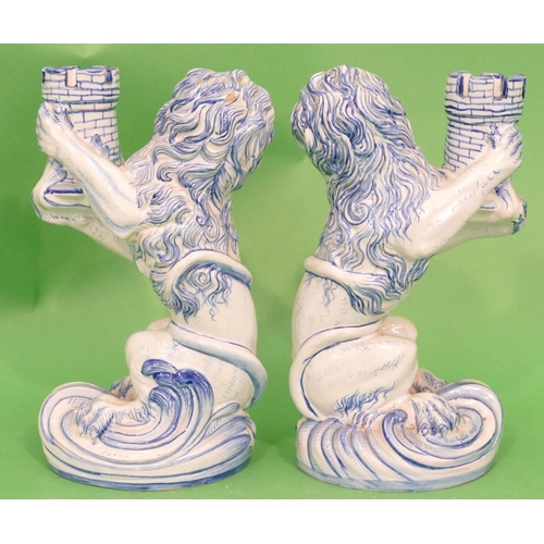 129 - A Pair of Continental Glazed Majolica Candlestick in form of seated lions holding turrets on blue an... 