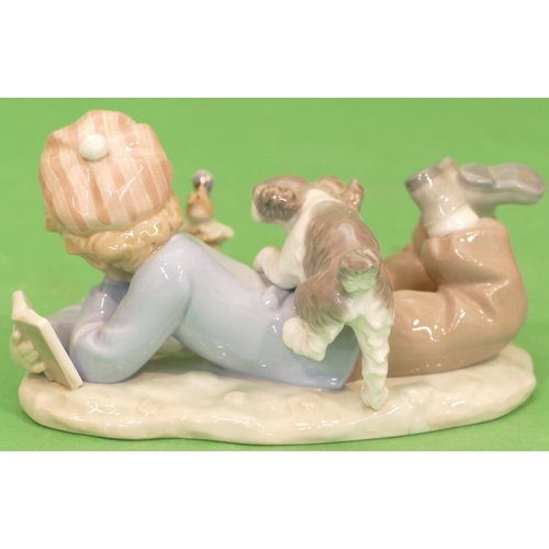 47 - A Lladro Group of a young boy resting on the ground reading a book with dog upon his back looking at... 