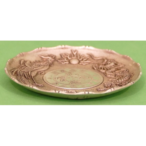 240 - An Oriental Silvered Dish having raised dragon decoration with inset coin to centre, 9cm diameter.