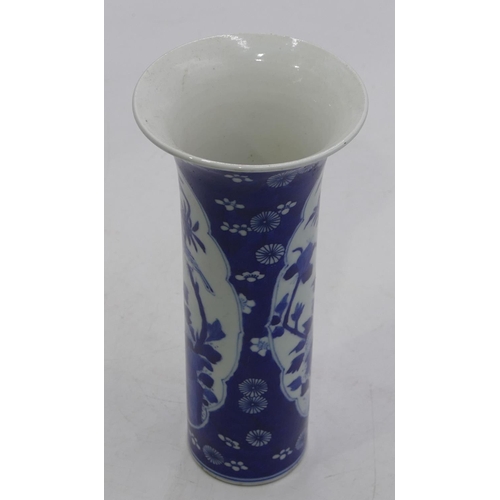 112 - An Oriental round cylindrical trumpet shaped vase on blue and white ground with floral and leaf deco... 