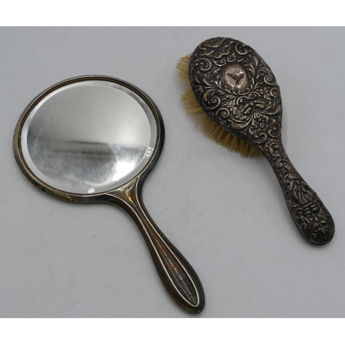 313 - A silver hand mirror and a silver mounted hair brush with embossed decoration (dented). (2).