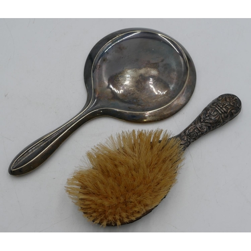 313 - A silver hand mirror and a silver mounted hair brush with embossed decoration (dented). (2).