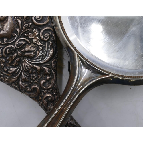 313 - A silver hand mirror and a silver mounted hair brush with embossed decoration (dented). (2).