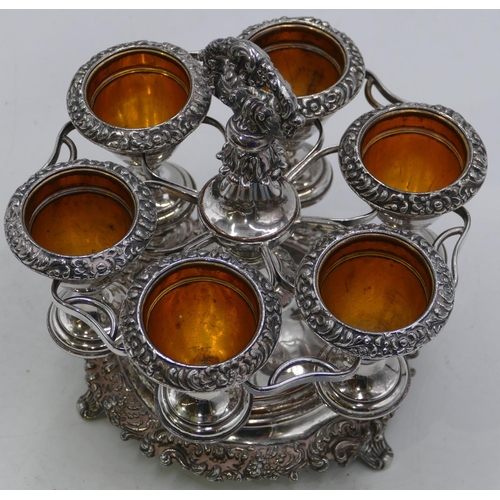 320 - A silver plated circular stand with centre carrying handle, mounted with 6 egg cups on 3 splayed fee... 