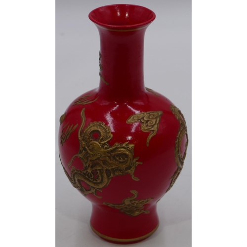 56 - An Oriental round bulbous thin necked trumpet shaped vase on red ground with raised gilt dragon deco... 