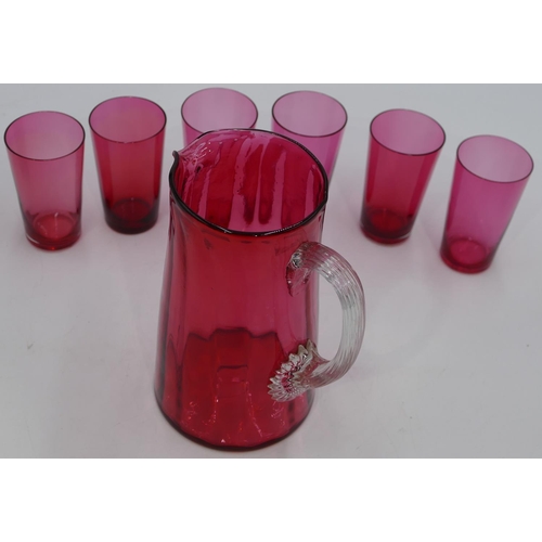 64 - A Cranberry glass round jug with clear reeded handle, 18cm high and 6 Cranberry beakers. (7)