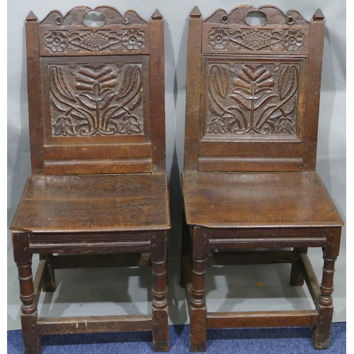 868 - A pair of 18th Century oak hall chairs with carved panel backs and floral leaf and scroll decoration... 