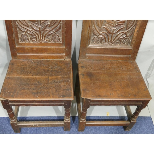 868 - A pair of 18th Century oak hall chairs with carved panel backs and floral leaf and scroll decoration... 