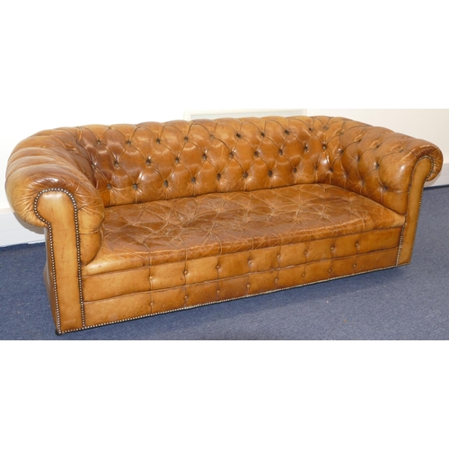 872 - A brown leather Chesterfield settee with buttoned seat, back and arms, part studded decoration, on c... 