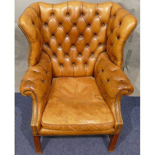 874 - A mahogany framed and brown leather wing back armchair with buttoned back, arms and wings, part stud... 