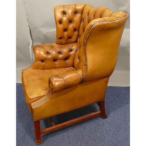 874 - A mahogany framed and brown leather wing back armchair with buttoned back, arms and wings, part stud... 