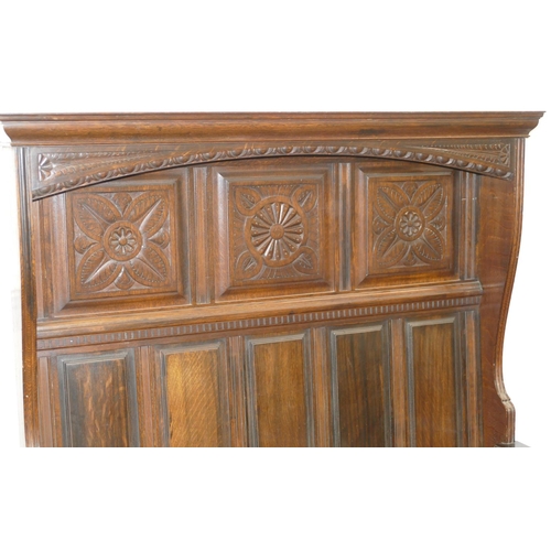 875 - An oak tall back settle with plain and carved panel back, hinged seat with further carved panels to ... 