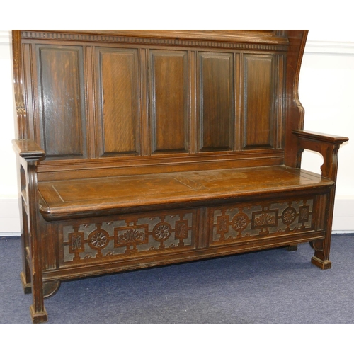 875 - An oak tall back settle with plain and carved panel back, hinged seat with further carved panels to ... 