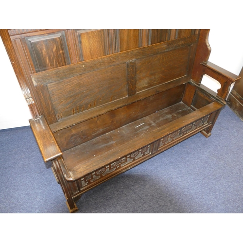 875 - An oak tall back settle with plain and carved panel back, hinged seat with further carved panels to ... 