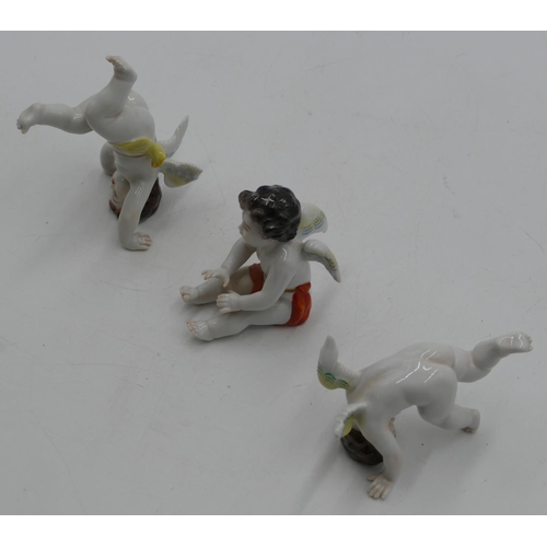 101 - A set of 3 Continental porcelain figures of cupids seated and doing handstands, largest 10.5cm high.... 