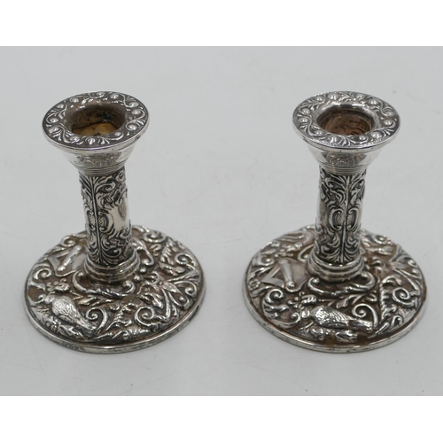 266 - A pair of Birmingham silver dwarf candlesticks with allover embossed bird, floral and scroll decorat... 