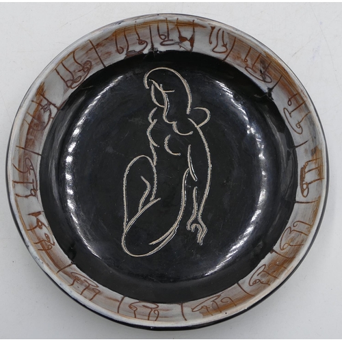 29 - A Continental glazed earthenware shallow round dish on black and brown ground with female nude to ce... 