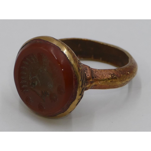 308 - A Roman style gilt ring set with a circular red stone engraved with a figurehead. Size Q