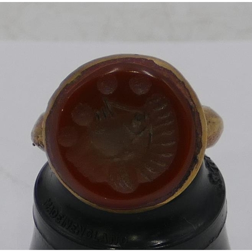 308 - A Roman style gilt ring set with a circular red stone engraved with a figurehead. Size Q