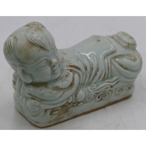 50 - An Oriental china pillow in the form of a reclining child on pale green ground,21cm long.