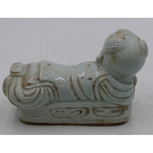 50 - An Oriental china pillow in the form of a reclining child on pale green ground,21cm long.