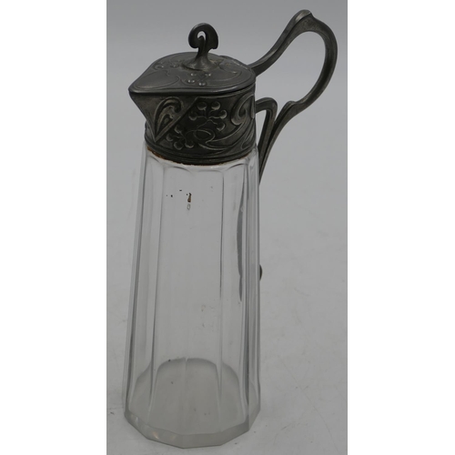 733 - An Arts & Crafts cut glass water jug with pewter neck, scroll handle and hinged lid with embossed fl... 