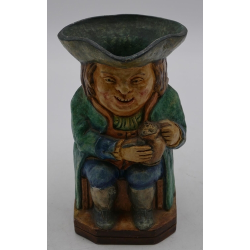 89 - A Compton pottery Toby jug in form of a seated gentleman wearing a green coat holding a jug, 18.7cm ... 