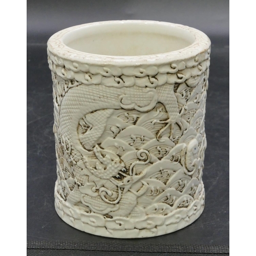 174 - An Oriental cylindrical brush pot on white ground with raised dragon and fish decoration, 11.6cm hig... 