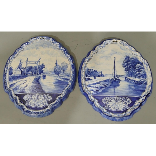 104 - A pair of Delft oval scallop shaped hanging plaques on blue and white ground depicting river landsca... 