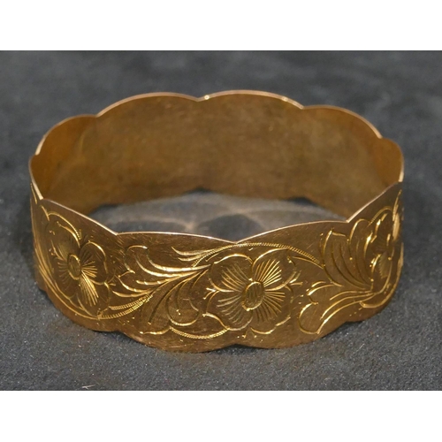 445 - A high carat gold bangle with scallop shaped rims, engraved with floral and leaf decoration, inner m... 