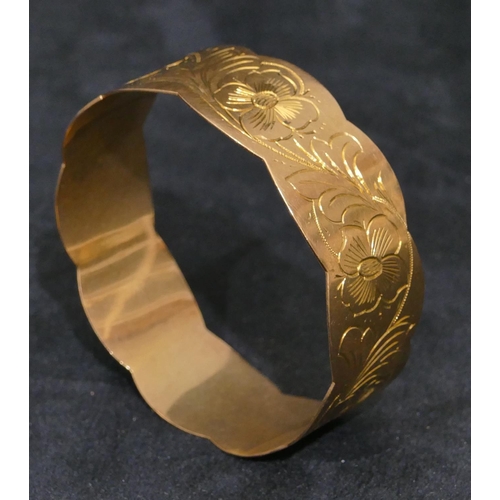 445 - A high carat gold bangle with scallop shaped rims, engraved with floral and leaf decoration, inner m... 