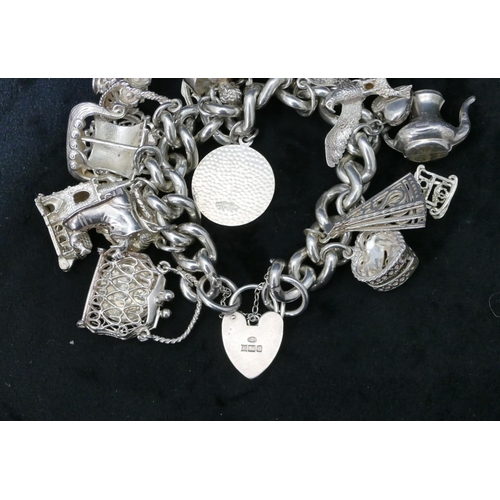 456 - A silver bracelet with padlock clasp, mounted with 17 charms, 139.6 grams