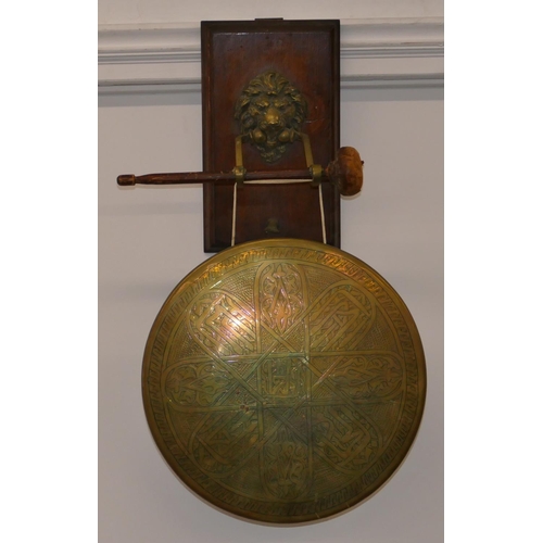 672 - A circular brass hanging gong with hammer mounted on oak panel with lion's head motif, gong 30cm dia... 