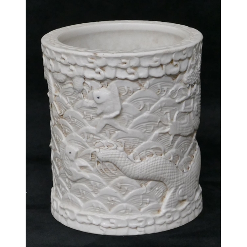 100 - An Oriental cylindrical brush pot on white ground with raised dragon and fish decoration, 12cm high