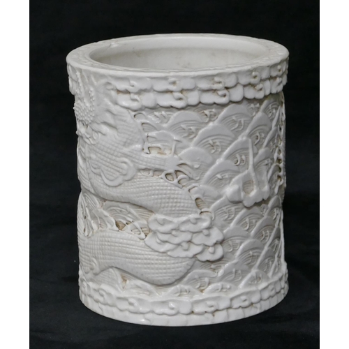 100 - An Oriental cylindrical brush pot on white ground with raised dragon and fish decoration, 12cm high