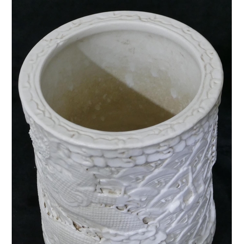 100 - An Oriental cylindrical brush pot on white ground with raised dragon and fish decoration, 12cm high