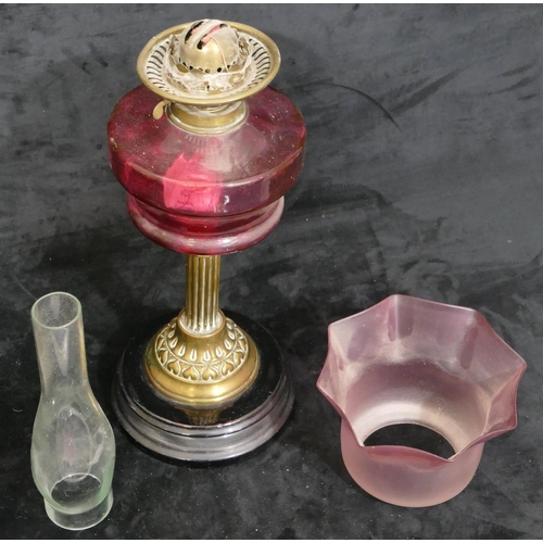 76 - A ruby glass duplex paraffin lamp with brass column stem on black glass circular base, with pink sha... 