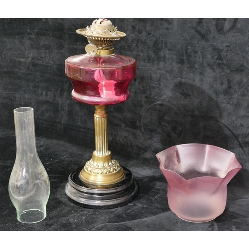 76 - A ruby glass duplex paraffin lamp with brass column stem on black glass circular base, with pink sha... 