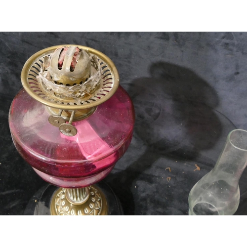 76 - A ruby glass duplex paraffin lamp with brass column stem on black glass circular base, with pink sha... 