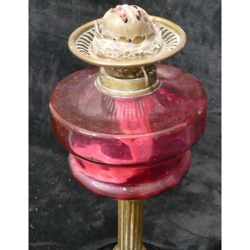 76 - A ruby glass duplex paraffin lamp with brass column stem on black glass circular base, with pink sha... 