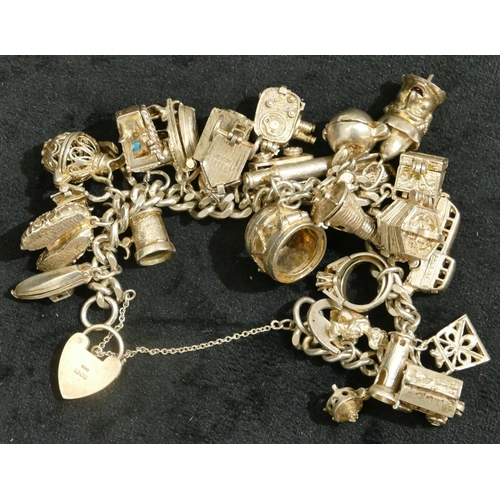 695 - A silver flat linked bracelet with padlock clasp, mounted with 25 silver charms, 121.4 grams