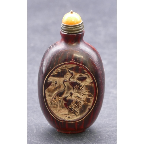 730 - An Oriental snuff bottle on red ground with oval panels depicting birds with stopper, 8.5cm high