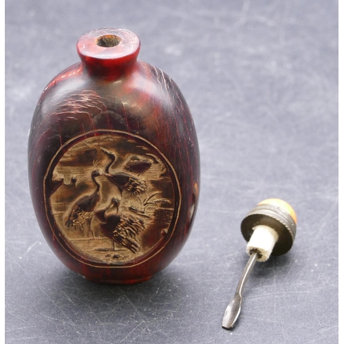 730 - An Oriental snuff bottle on red ground with oval panels depicting birds with stopper, 8.5cm high