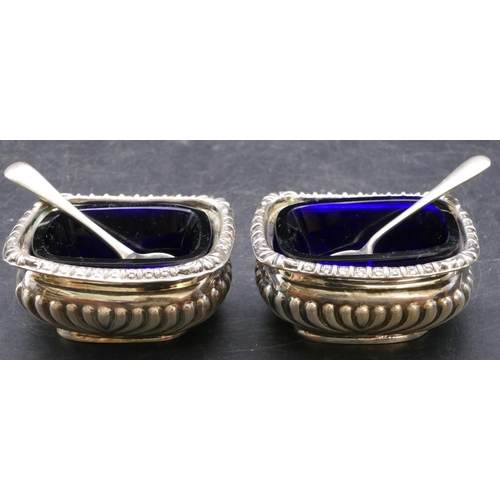 372 - A pair of Chester silver rectangular bulbous shaped salts with blue glass liners, half embossed reed... 