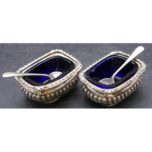 372 - A pair of Chester silver rectangular bulbous shaped salts with blue glass liners, half embossed reed... 