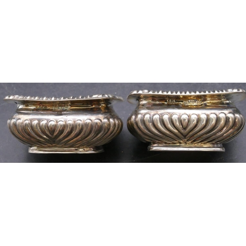 372 - A pair of Chester silver rectangular bulbous shaped salts with blue glass liners, half embossed reed... 