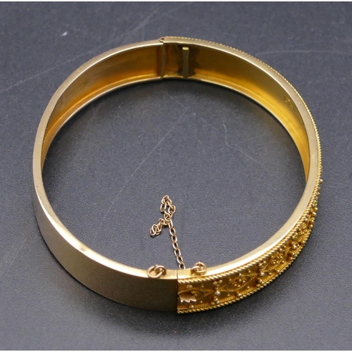 808 - A 15ct gold hinged bangle with raised decoration, 13.1 grams